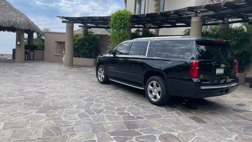 Black Moonline Cabo Chevrolet Suburban parked in a stone-paved villa driveway in front of a wooden pergola