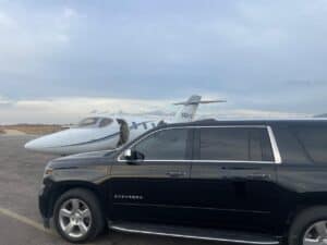 Black Moonline Cabo Chevrolet Suburban parked beside a private jet on an airport apron