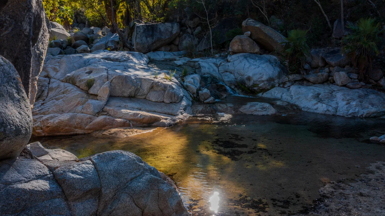 Clear pools between smooth granite boulders on a mountain stream in the Sierra de la Laguna, lit by low sun — photo by Adrián De Antoni