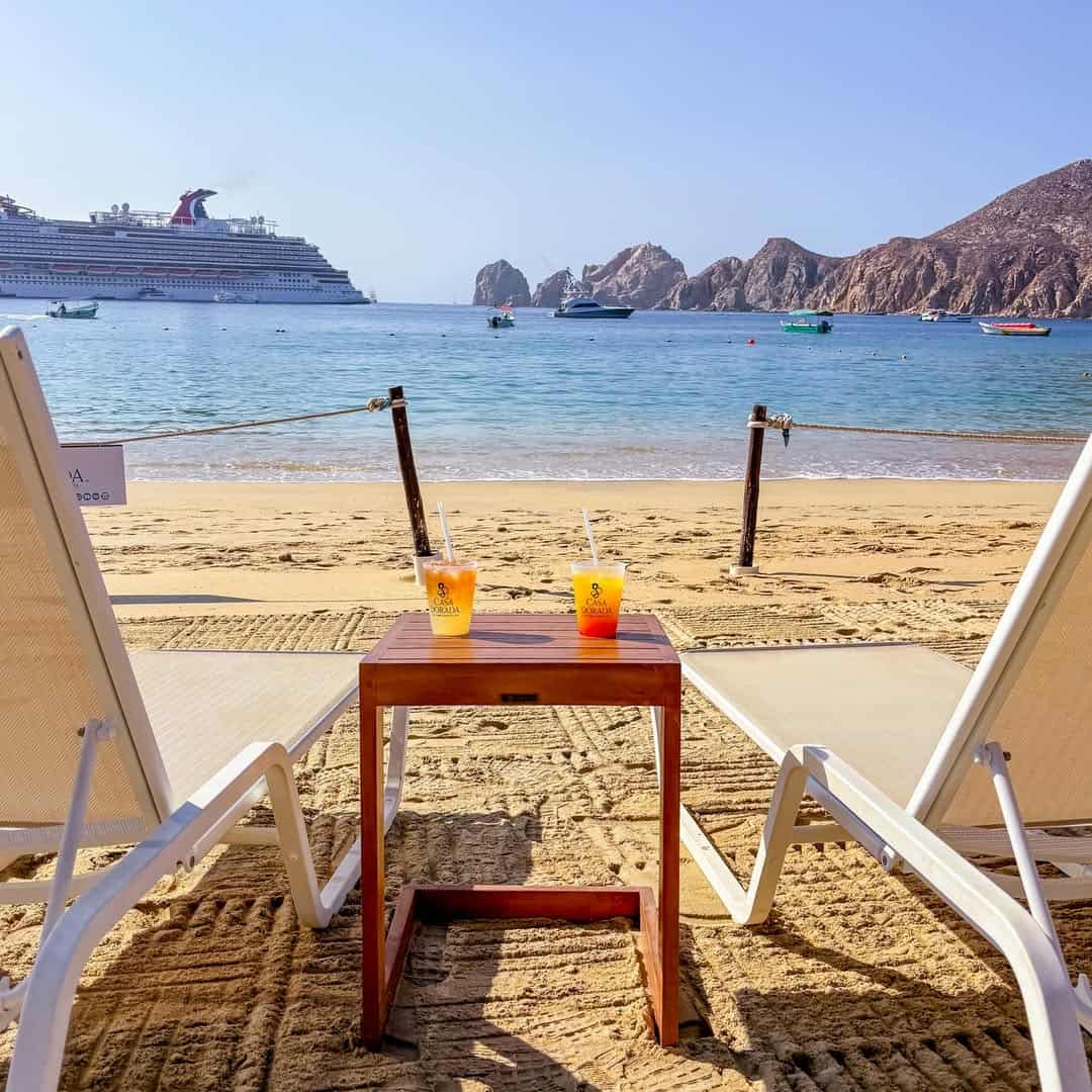 Two beach chairs and tropical drinks facing Land’s End from Médano Beach.