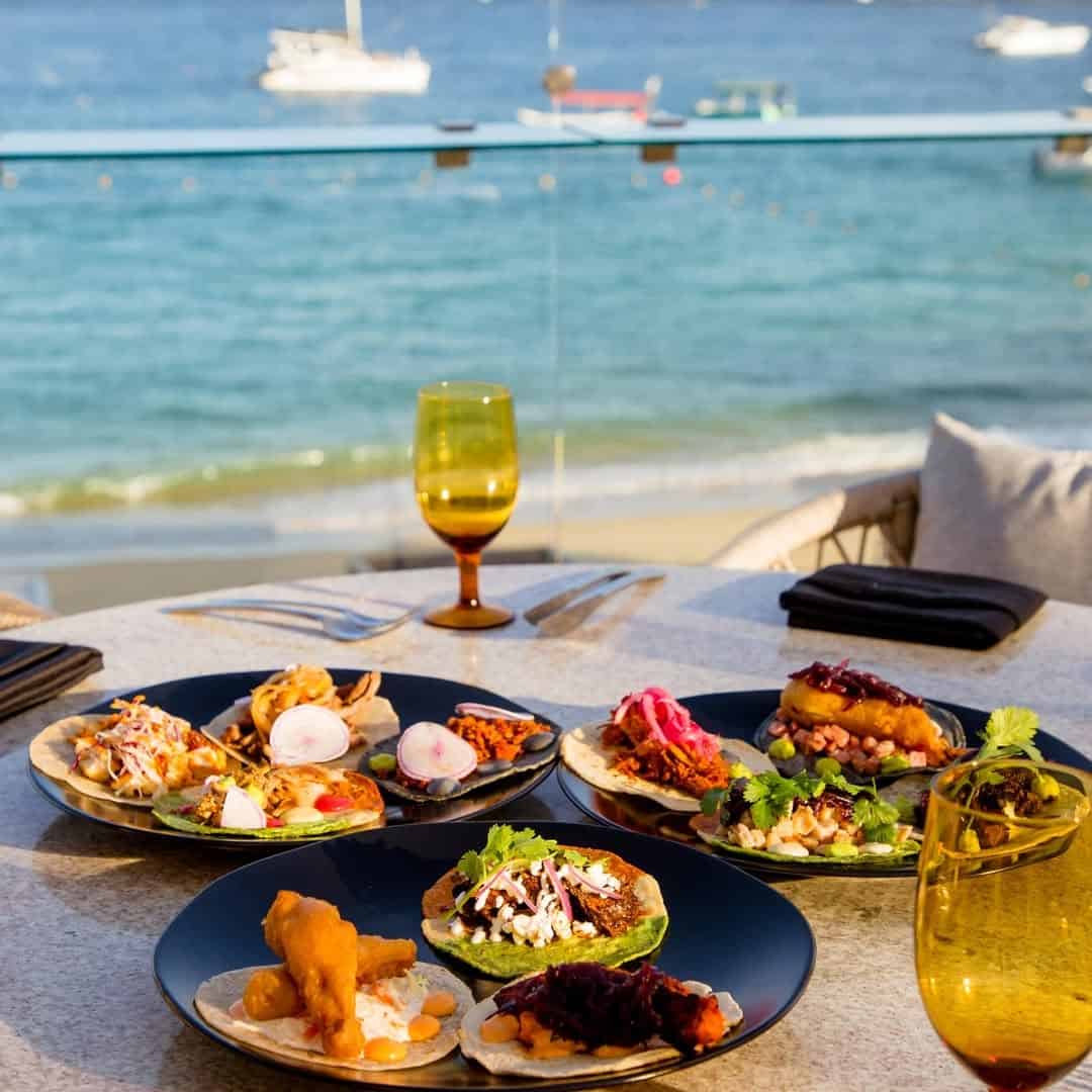 An assortment of tacos arranged on a table beside the ocean.